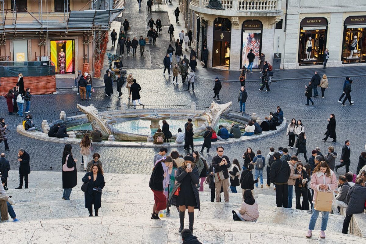 Huardière Bustling crowd at Piazza di Spagna, Rome, showcasing vibrant city life around the Barcaccia Fountain.