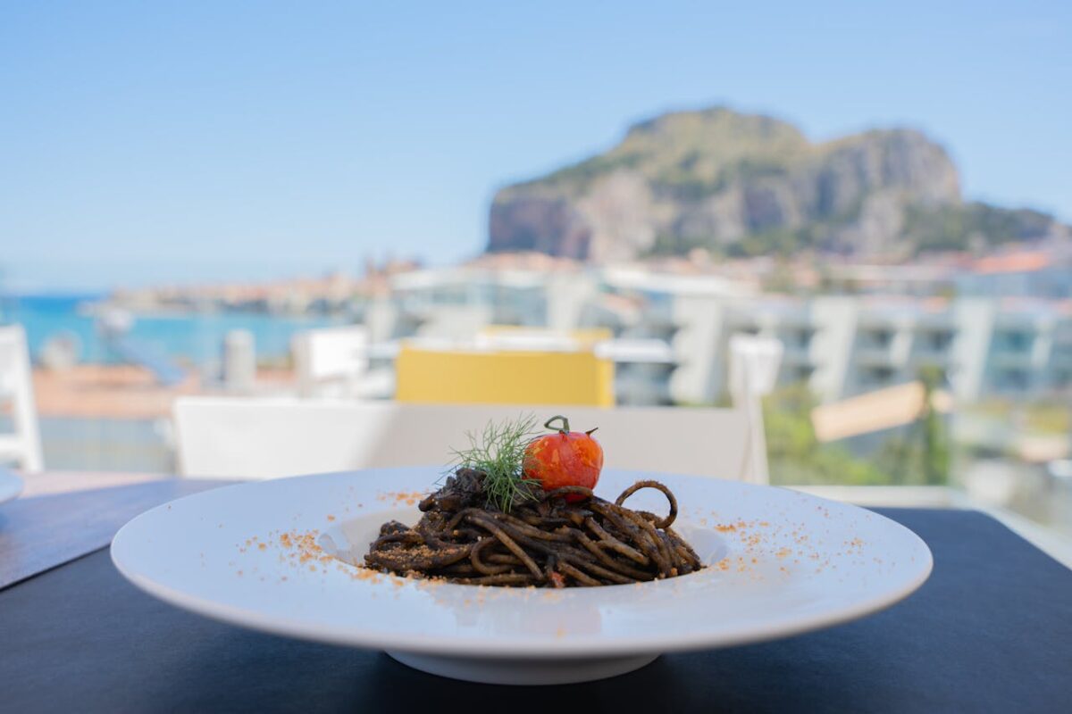 Offres Plate of squid ink pasta with tomato and herbs, set against a beautiful seaside view.