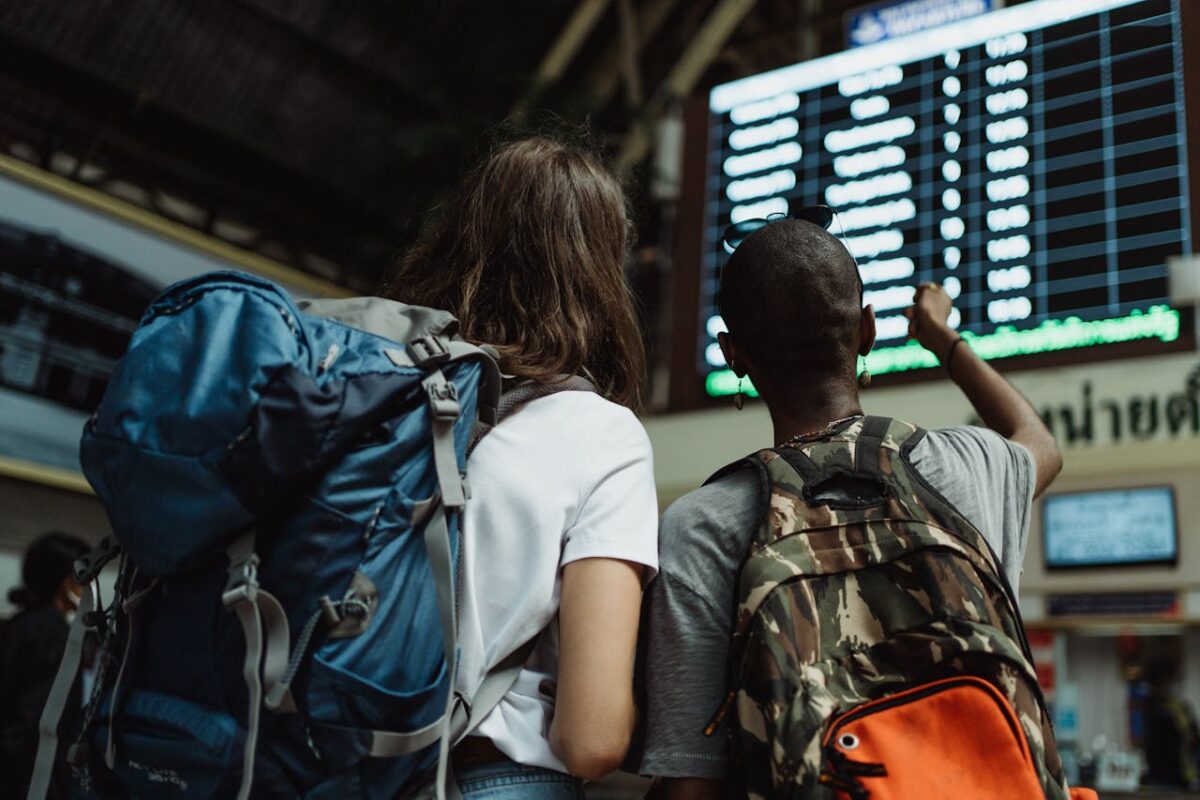Huardière Two backpackers checking the digital board at a train station for travel information.